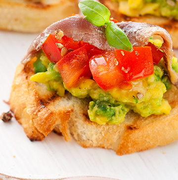 Toastjes gegarneerd met avocado, een brunoise van tomaten, ansjovis en basilicum.